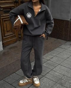 Détail du survêtement gris foncé montrant la texture du sweat à col zippé et l'écusson