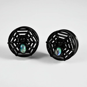 Close-up of black spider ear gauge featuring iridescent shell inlay and spider web detail