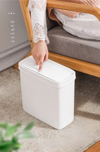 Narrow white press-top trash can with vertical stripes placed next to a modern sofa
