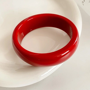 Vue macro d'un bracelet large en résine rouge brillant sur une assiette blanche