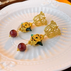 Macro detail of vintage golden earrings featuring deep green gem and red bead charms