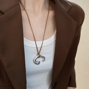 Close-up of irregular C-shaped silver pendant necklace worn with brown cord on a model