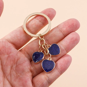 Detail of hand holding three blue glitter heart keychains with golden alloy chains