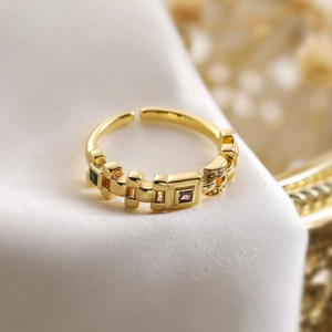 Macro shot of gold geometric ring with green and purple square zircons on white silk