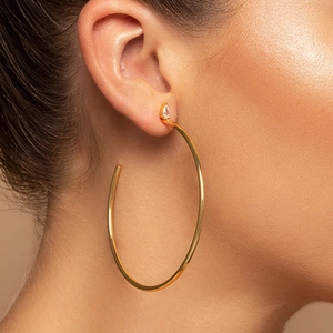 Detail of gold C-shaped hoop earrings with a teardrop-shaped gemstone on model ear