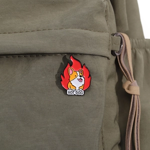 Close-up of a cute Corgi hot dog enamel pin badge on a green canvas backpack fabric