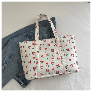 Close-up of a white tote bag featuring red cherry prints and small front pocket