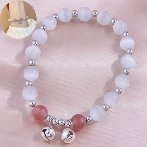 Detail of beaded bracelet with cat eye stones and small silver bells on pink silk fabric