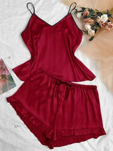 Flat lay of satin pajama set in burgundy with black lace trim and bow on white texture
