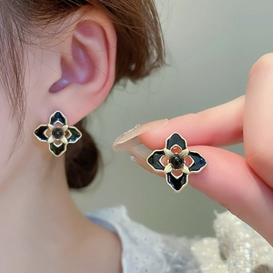 Close-up of black floral stud earrings with gold trim and velvet texture on ear