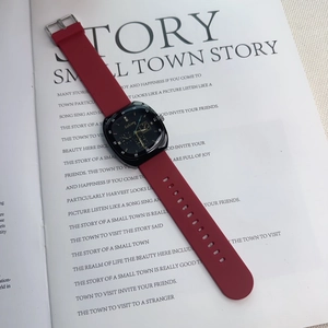 Detail of square black dial with gold markers and red silicone strap on a magazine