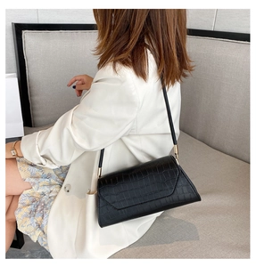 Detail of a black crocodile texture baguette bag worn with a white blazer for a chic look
