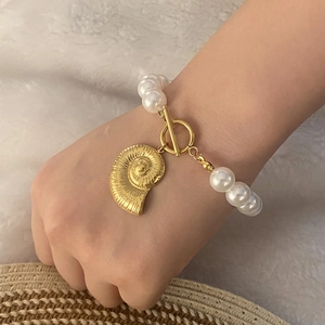 Elegant pearl necklace with gold nautilus pendant and T-bar clasp worn by a model