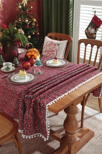 Detail of red plaid Christmas tablecloth featuring snowflake patterns and white pom pom tassels
