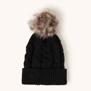 Detail shot of black cable knit beanie with fluffy faux fur pompom on plain background