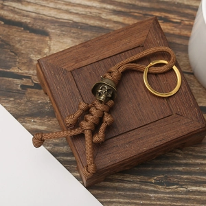 Handmade paracord skull keychain with brass helmet bead on a rustic wooden box