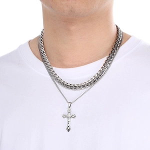 Close-up of silver stainless steel Cuban chain and layered cross pendant on male model