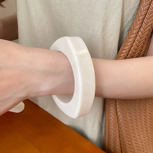 Nahaufnahme eines minimalistischen, klobigen elfenbeinfarbenen Resin-Armreifs am Handgelenk