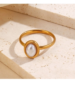 Detail shot of a golden oval pearl ring displayed on minimalist beige travertine stone