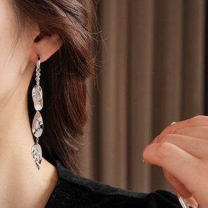 Détail de boucles d'oreilles pendantes argentées avec pampilles en forme de feuille sur mannequin
