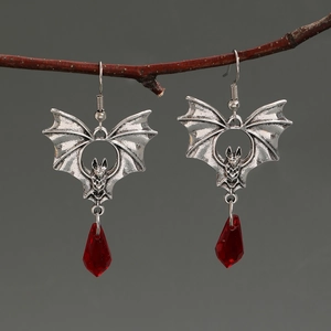 Close-up of gothic black bat earrings with red crystal teardrops on a branch