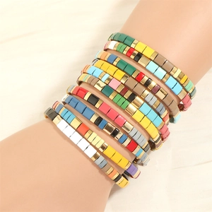 Detail of colorful enamel Tila tile elastic bracelets with gold accent beads in a stack