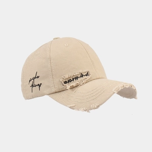 Close-up of distressed beige cotton baseball cap with vintage embroidery and torn details