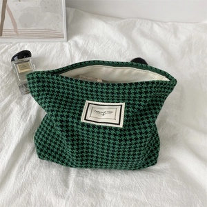 Detail of green houndstooth cosmetic bag with zipper and branded label on white background