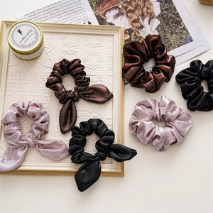 Flat lay of elegant fabric hair scrunchies with bows and metal luster on a decorative tray