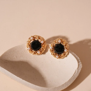 Boucles d'oreilles vintage dorées avec pierre noire et perles blanches sur plateau céramique