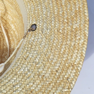 Dettaglio cappello di paglia con occhielli in metallo dorato e catena di perle bianche