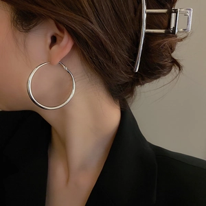 Minimalist silver hoop earrings with a large circular design shown on a model