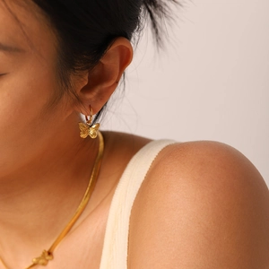 Close-up of golden butterfly earrings and matching snake chain necklace on a model