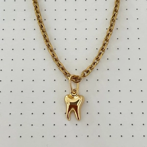 Detailed close-up of a polished gold-plated tooth pendant on a thick link chain necklace