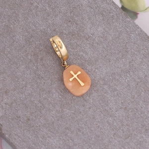 Détail macro du pendentif en pierre naturelle et croix dorée sur fond de pierre grise