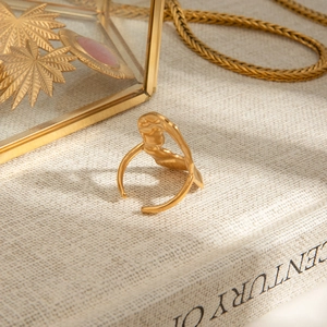 Detailed macro view of an 18k gold wave-textured adjustable ring on aesthetic background
