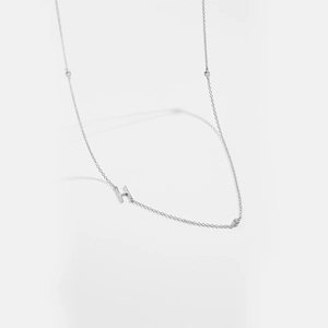 Macro detail of silver necklace featuring an H letter pendant with sparkling crystals