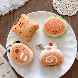 Macro shot of plush food charms including burgers and bread arranged in a white decorative tray