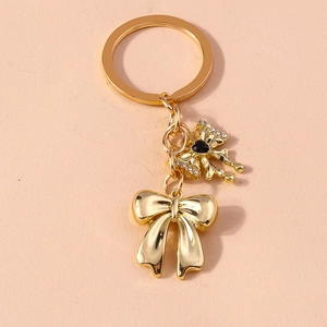 Elegant gold bow keychain with pearls and rhinestones on a minimalist beige background