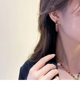 Detail of luxury gold plated earrings with colorful rectangular zirconia stones on model