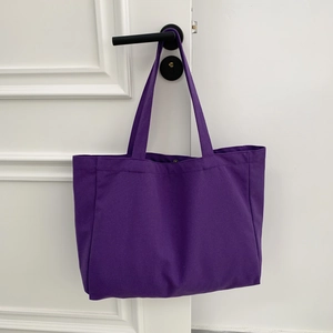 Detail view of large purple canvas tote bag hanging on a door handle in a simple setting