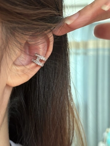 Close-up of a silver H-shaped ear cuff with sparkling zircon stones on a model's ear