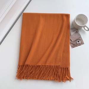 Detailed close-up of folded orange cashmere-feel scarf with fringes on white background