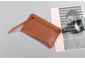 Detailed view of a brown leather wristlet wallet with zipper and handle on a desk