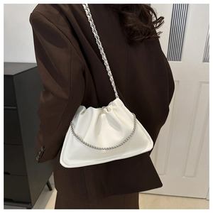 Detail of white leather cloud bag with silver chain strap worn by model in brown blazer