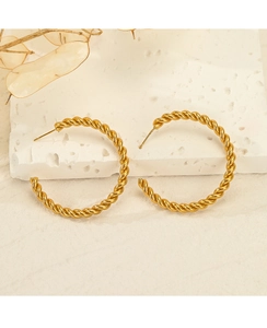 Macro shot of gold-plated twisted hoop earrings on a textured stone decorative background