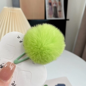 Detailed view of green faux fur pom-pom hair clip on a white cloud display card