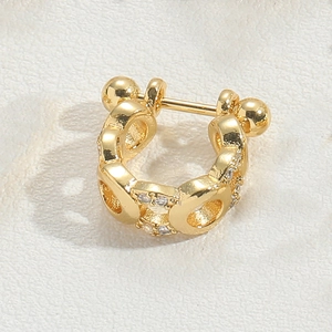 Macro shot of a golden C-shaped ear cuff with embedded clear gemstones on a textured surface