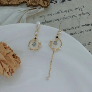 Detail of asymmetric celestial star and moon earrings with pearls and blue cubic zirconia
