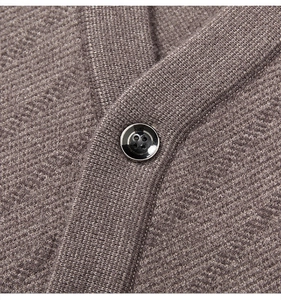 Nahaufnahme der Stricktextur und des glänzend schwarzen Knopfes an der braunen Weste